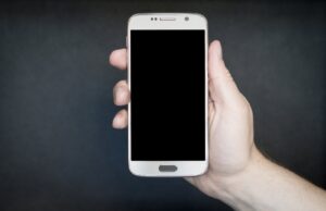 Mano sosteniendo un teléfono móvil de pantalla oscura sobre un fondo gris