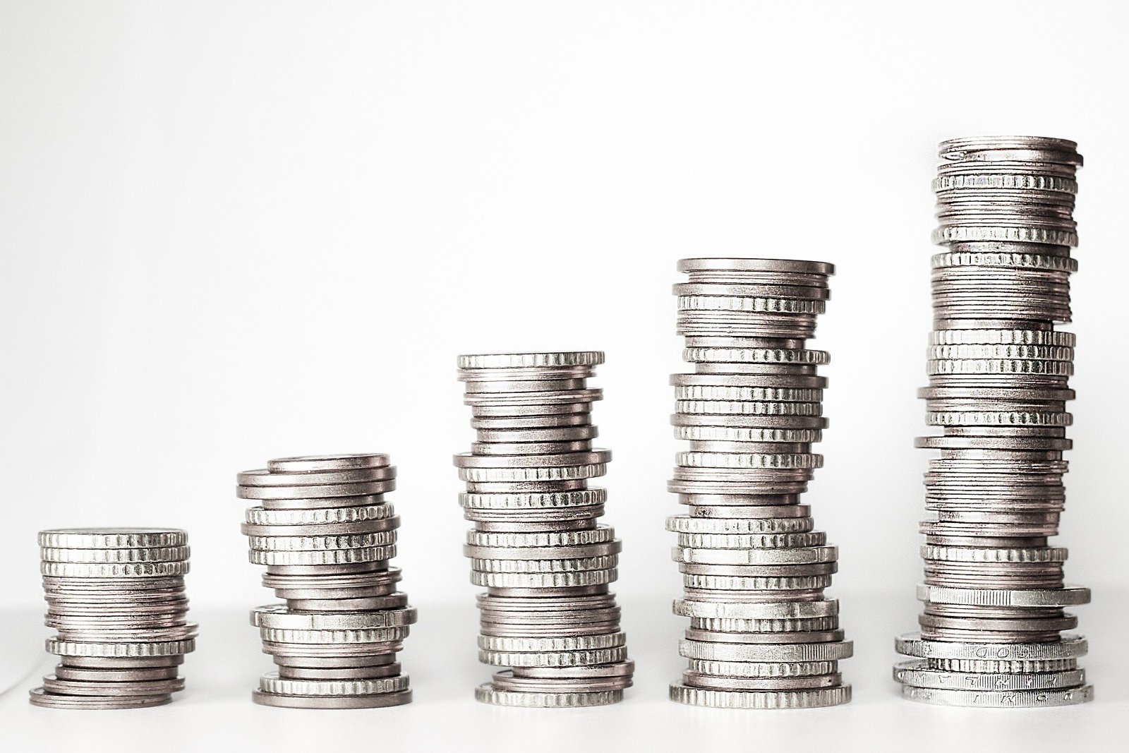 Cinco pilas de monedas de diferentes alturas sobre un fondo blanco